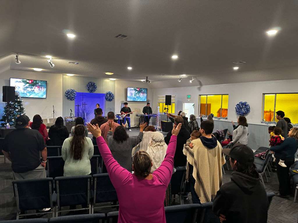 Congregational worship: Congregation members stand with hands raised in worship as musicians lead from the front of the church during a Christmas service.
